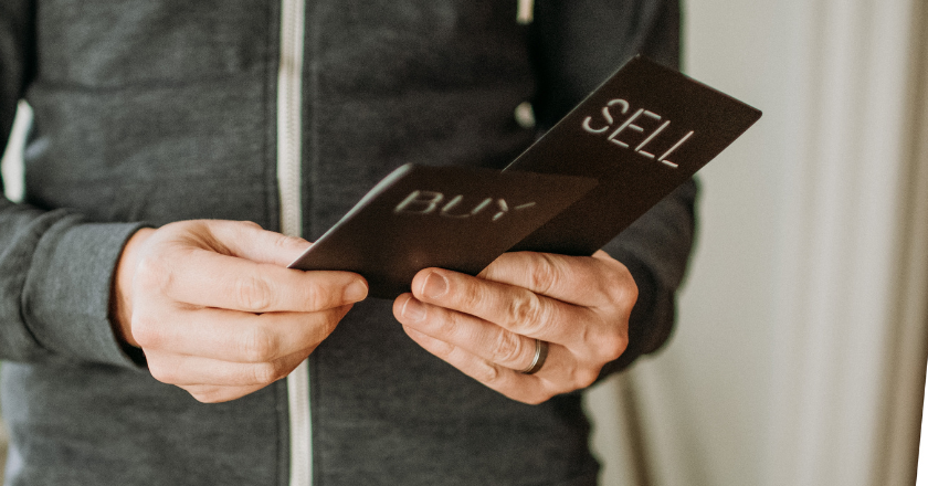 A man holding two signs, one reading sell, one reading buy